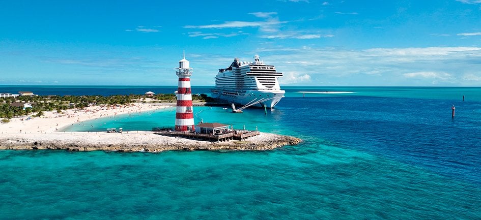 A cruise ship docked near a tropical island with a red-and-white lighthouse | MSC Cruises A cruise ship docked near a tropical island with a red-and-white lighthouse | MSC Cruises