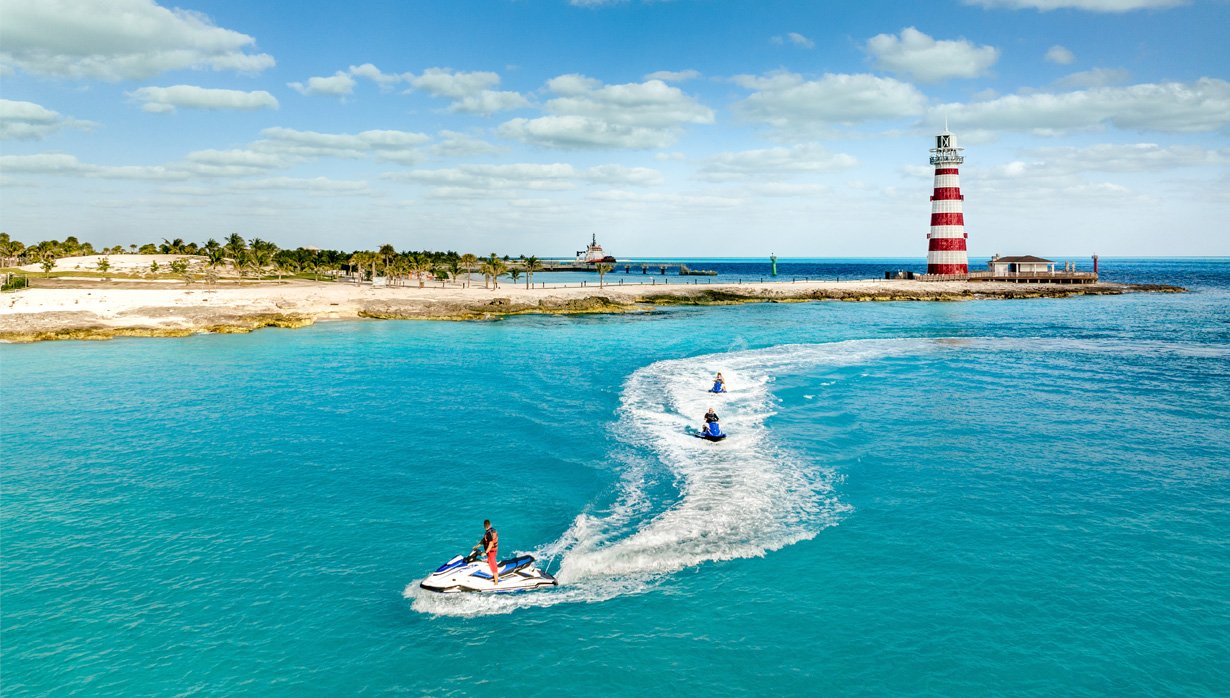 Jet skis gliding on turquoise waters near a striped lighthouse on a tropical island | MSC Cruises