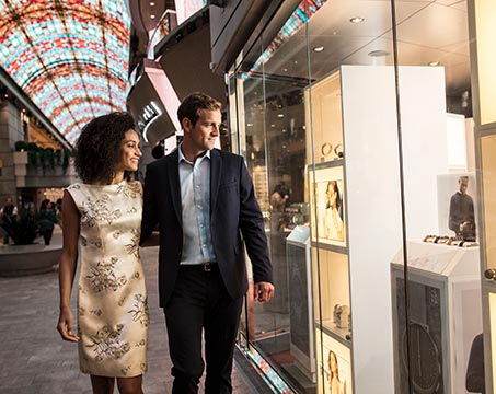 Couple strolling past luxury shops under a vibrant glass ceiling | MSC Cruises