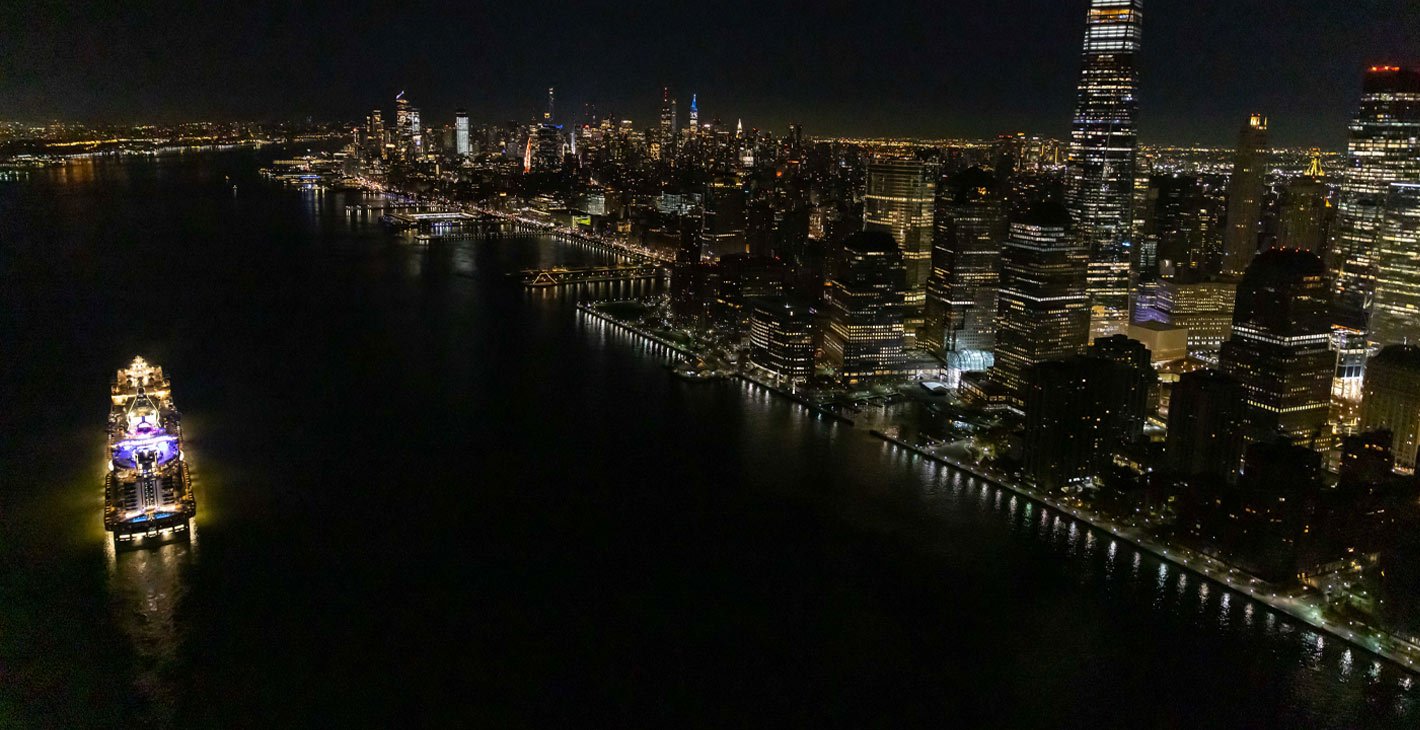 An illuminated MSC cruise ship sailing near New York City's skyline at night | MSC Cruises
