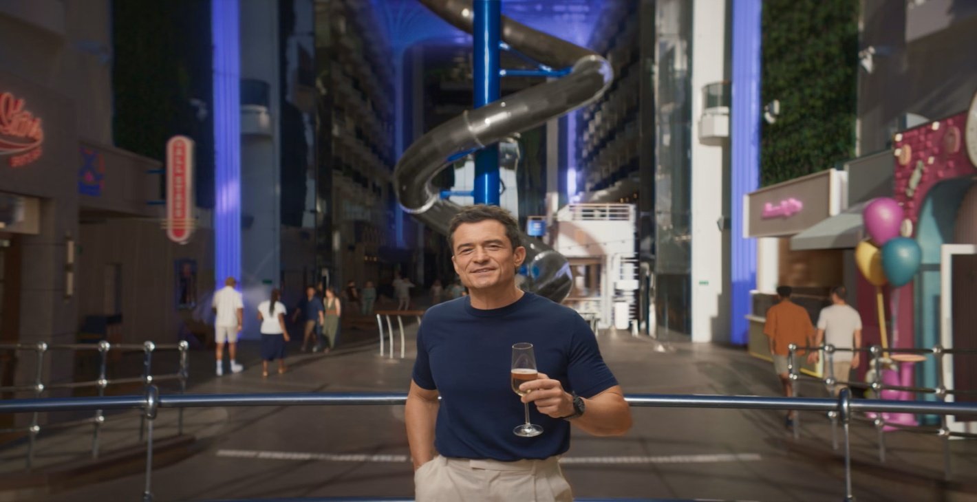 A man holding a champagne glass in a vibrant cruise ship promenade with a spiral slide | MSC Cruises