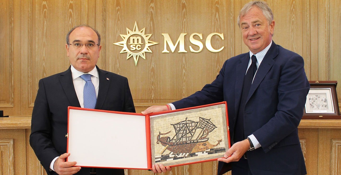 Two individuals presenting a framed mosaic of an ancient ship in front of an MSC logo | MSC Cruises