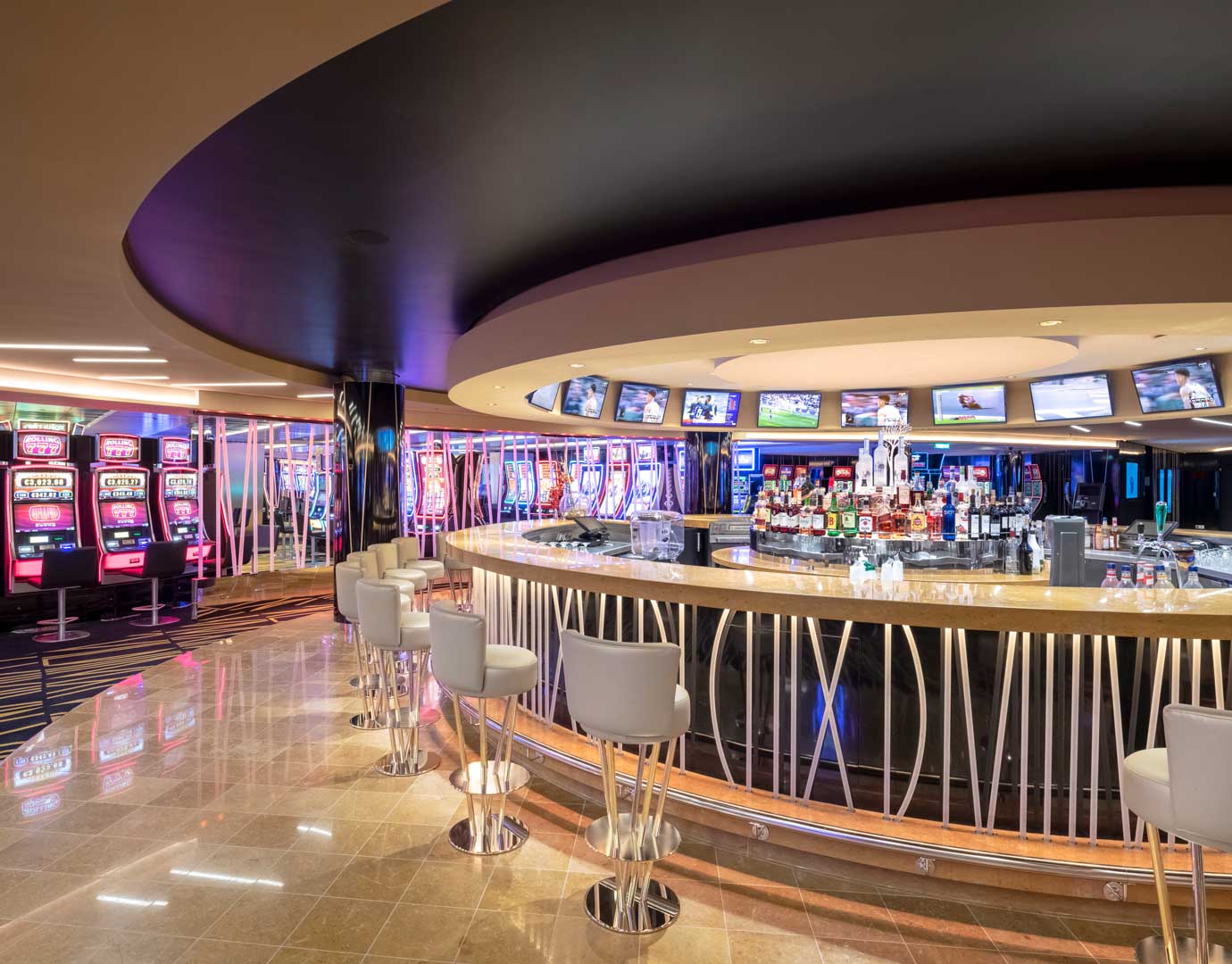 A stylish onboard bar with slot machines and multiple TV screens in a luxurious setting | MSC Cruises A stylish onboard bar with slot machines and multiple TV screens in a luxurious setting | MSC Cruises